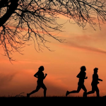 Orang berolahraga di taman dengan latar belakang matahari terbit, mencerminkan gaya hidup sehat.